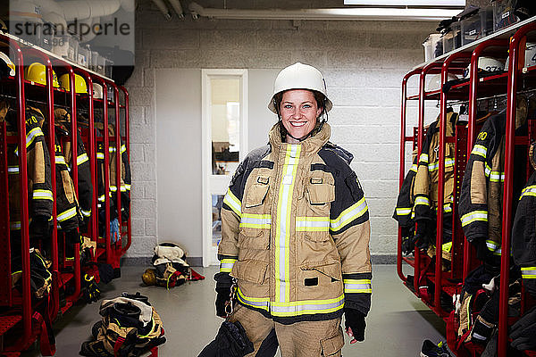 Porträt einer lächelnden Feuerwehrfrau  die in der Umkleidekabine der Feuerwache steht