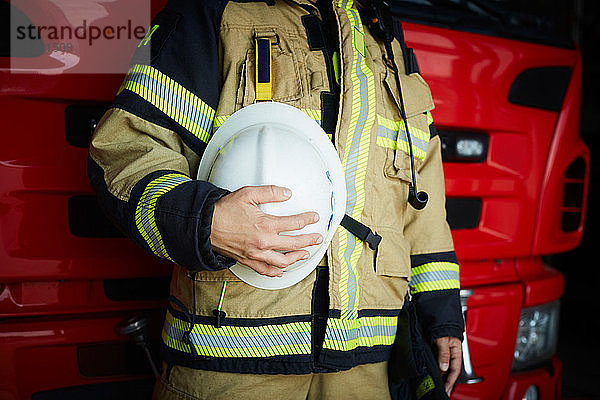 Mittelteil einer weiblichen Feuerwehrfrau  die einen Helm hält  während sie auf der Feuerwache steht