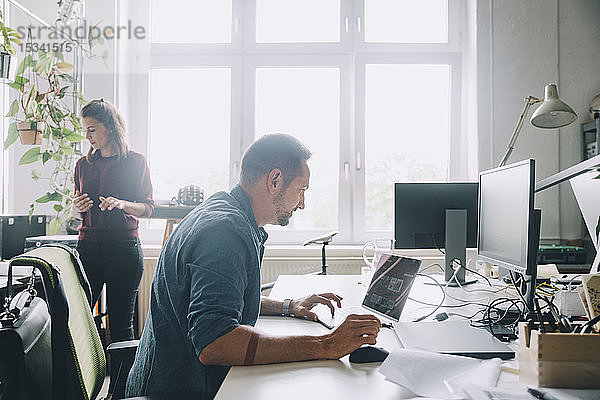 Seitenansicht eines Geschäftsmannes mit Laptop am Schreibtisch im Kreativbüro