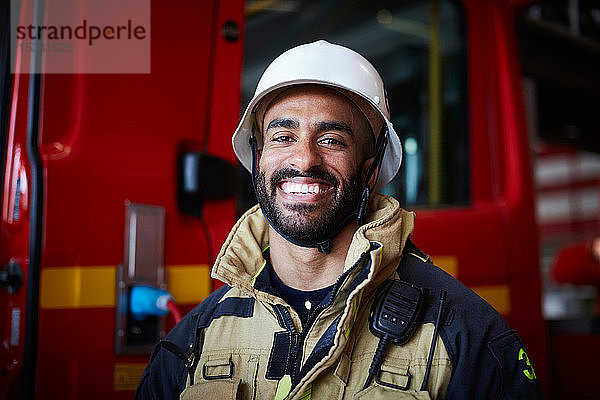 Porträt eines lächelnden Feuerwehrmannes mit Helm auf der Feuerwache stehend