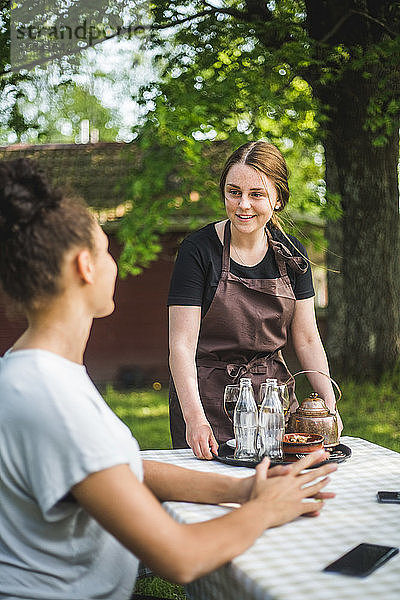 Lächelnde Kellnerin betrachtet im Restaurant sitzenden Kunden