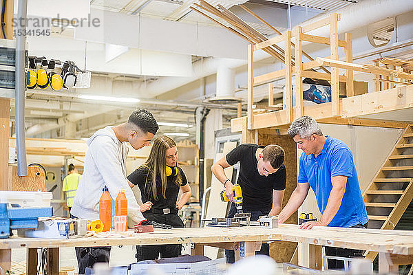 Zimmermann und Auszubildende  die während der Ausbildung zusehen  wie ein Mann eine Bohrmaschine an der Werkbank bedient