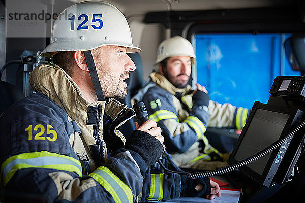 Feuerwehrmann spricht am Mikrofon  während er mit einem Kollegen im Feuerwehrauto sitzt