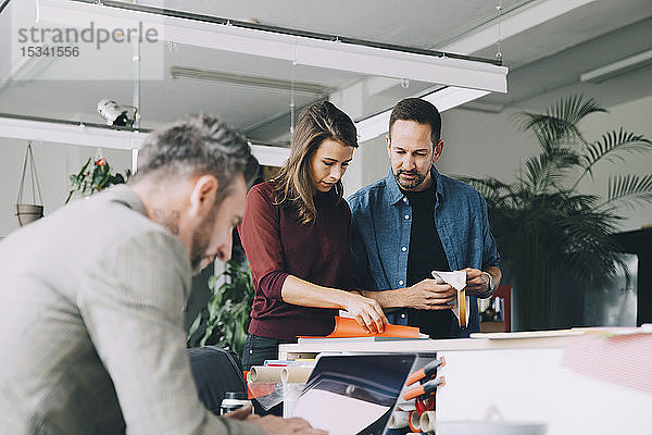 Geschäftsmann und Geschäftsfrau diskutieren  während ein männlicher Kollege im Kreativbüro am Laptop arbeitet