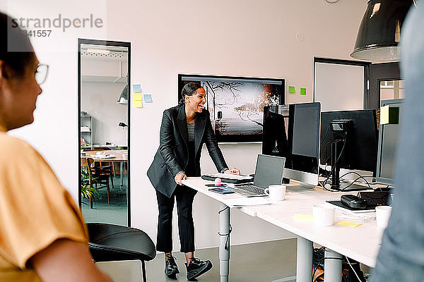 Lächelnde Unternehmerin schaut weg  während sie bei einer Bürobesprechung am Schreibtisch steht