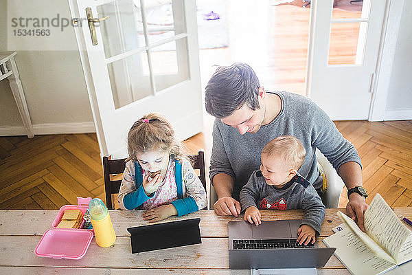 Hochwinkelansicht eines lächelnden Vaters mit einem niedlichen Sohn  der neben der Tochter sitzt  mit einem digitalen Tablett am Tisch
