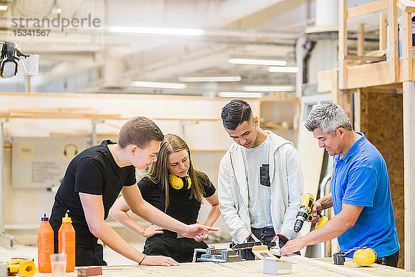 Männlicher Ausbilder erklärt Auszubildenden an der Werkbank den Bohrer auf einem Brett