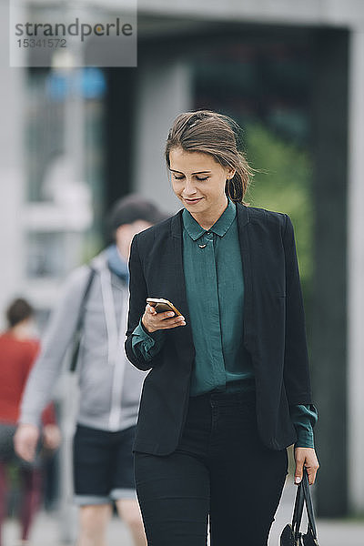 Selbstbewusste Geschäftsfrau benutzt Smartphone beim Gehen auf der Straße in der Stadt