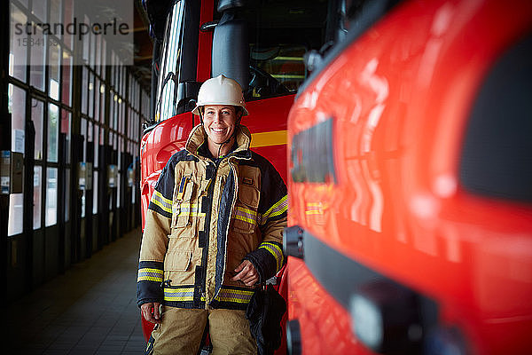 Porträt einer lächelnden Feuerwehrfrau  die in der Feuerwache beim Löschfahrzeug steht