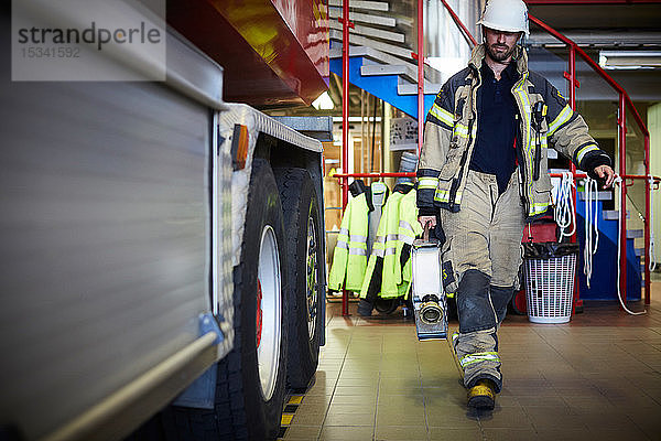 Feuerwehrmann hält Feuerwehrschlauch in voller Länge in der Hand  während er an einem Feuerwehrfahrzeug am Bahnhof vorbeigeht