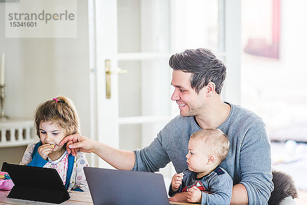 Lächelnder Vater sitzt mit seinem Sohn zusammen  während er ein Mädchen berührt  das sich zu Hause einen Film auf einem digitalen Tablet anschaut