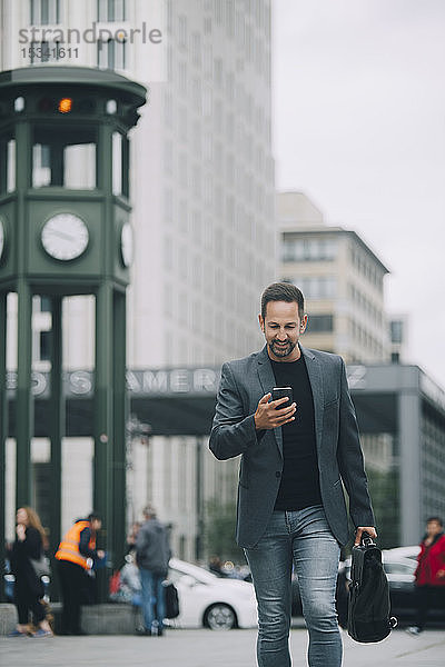 Reifer Geschäftsmann benutzt Mobiltelefon beim Gehen auf der Straße in der Stadt