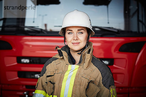 Porträt einer weiblichen Feuerwehrfrau mit Helm gegen Feuerwehrauto in der Feuerwache