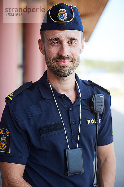 Porträt eines lächelnden Polizisten in Uniform  der vor der Polizeistation steht