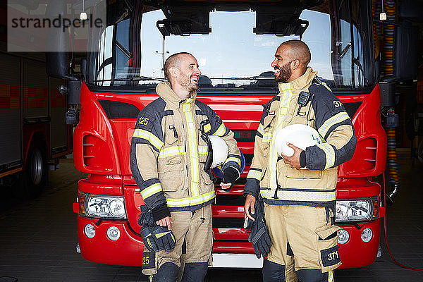 Fröhliche Feuerwehrleute unterhalten sich  während sie in der Feuerwache vor dem Löschfahrzeug stehen