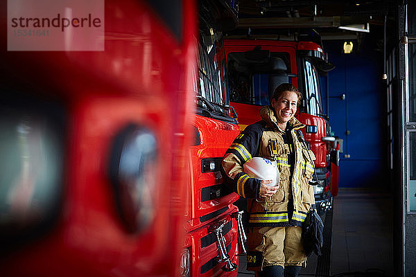 Porträt eines lächelnden Feuerwehrmannes mit Helm  der in der Feuerwache beim Löschfahrzeug steht