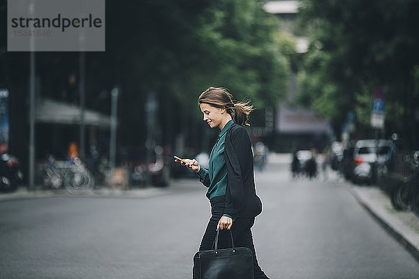 Selbstbewusste Geschäftsfrau benutzt Smartphone beim Überqueren der Straße in der Stadt