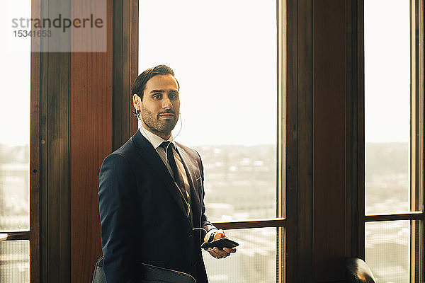 Porträt eines selbstbewussten Finanzberaters mit Smartphone vor dem Fenster einer Anwaltskanzlei