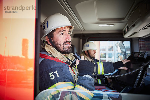 Mittlerer erwachsener Feuerwehrmann spricht am Mikrofon  während er mit seinem Kollegen im Feuerwehrauto sitzt