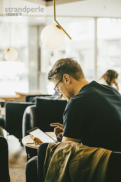 Seitenansicht eines Mannes  der ein digitales Tablet benutzt  während er im Restaurant sitzt
