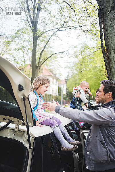 Vater gestikuliert gegenüber Mädchen  das auf Auto sitzt