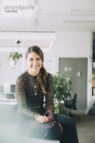 Porträt einer lächelnden Geschäftsfrau  die in einem kreativen Büro am Tisch sitzt