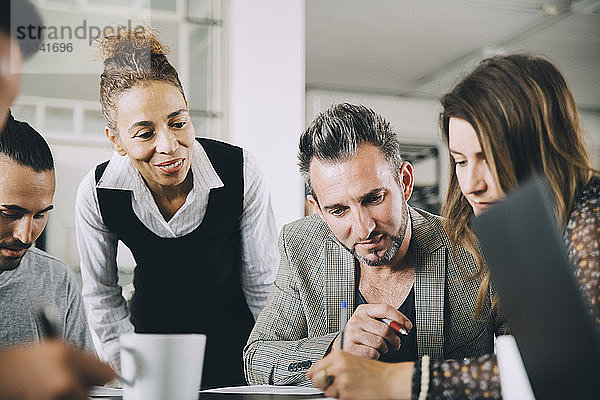 Kreative Geschäftsleute schauen auf Kolleginnen  die im Büro am Tisch schreiben