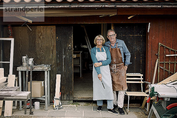 Ganzflächiges Porträt selbstbewusster älterer Mitarbeiter  die am Eingang zum Baumarkt stehen