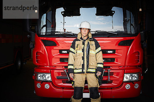 Porträt einer weiblichen Feuerwehrfrau  die in der Feuerwache vor dem Löschfahrzeug steht