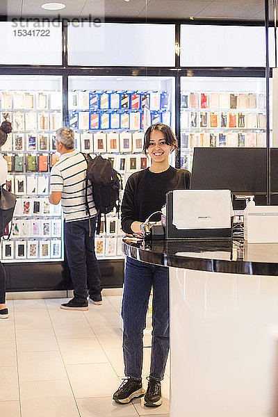 Porträt einer selbstbewussten Verkäuferin in voller Länge  die an der Kasse gegen Kunden im Laden steht