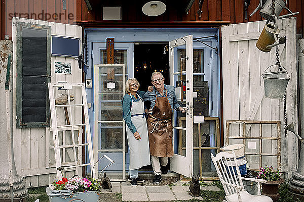Ganzflächiges Porträt selbstbewusster älterer Mitarbeiter  die an der Tür eines Eisenwarenladens stehen