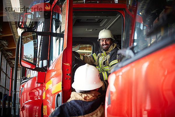 Lächelnder Feuerwehrmann im Gespräch mit einem Kollegen  während er im Feuerwehrauto der Feuerwache sitzt