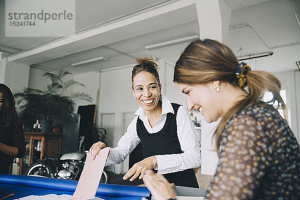 Lächelnde Geschäftsfrau schaut eine Kollegin an  die in einem kreativen Büro arbeitet