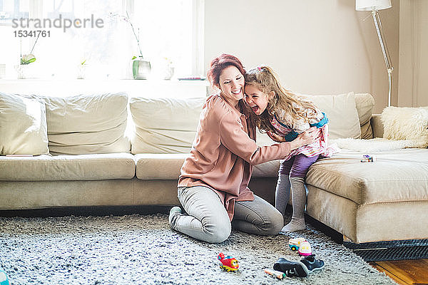 Lächelnde Frau umarmt Tochter  die zu Hause auf dem Sofa sitzt