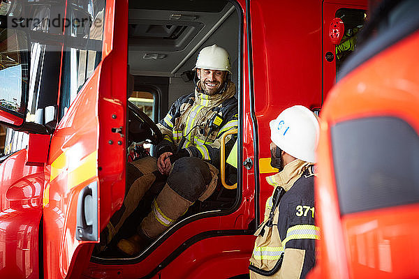 Feuerwehrmann im Gespräch mit einem Kollegen  während er im Feuerwehrauto der Feuerwache sitzt