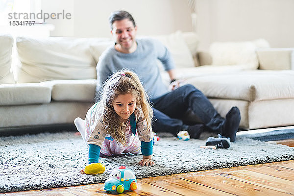 Glücklicher Mann sieht Tochter an  die zu Hause mit Spielzeug spielt