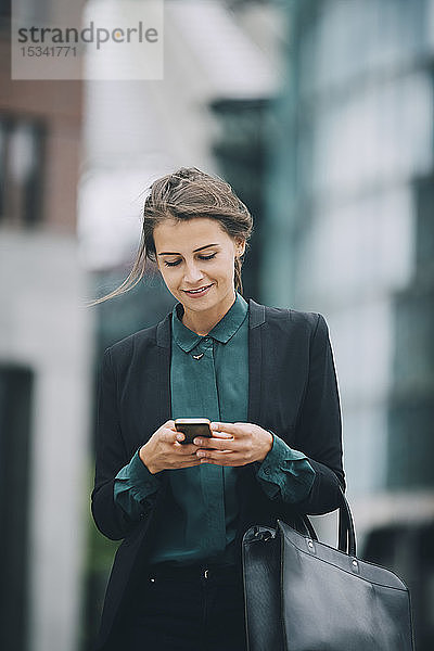 Selbstbewusste Geschäftsfrau sendet bei einem Spaziergang in der Stadt Textnachrichten über ein Smartphone