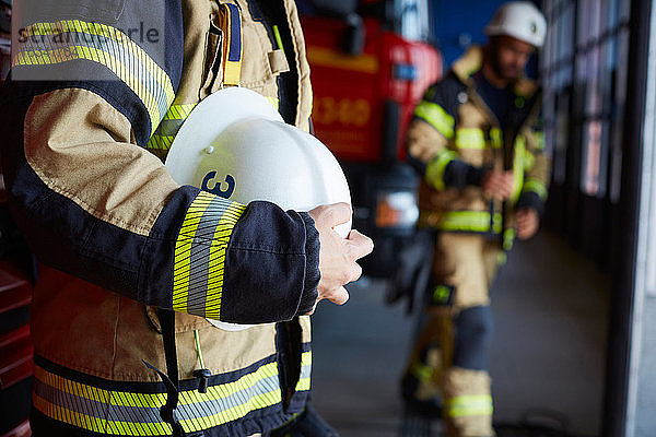 Mittelteil einer weiblichen Feuerwehrfrau mit Schutzhelm auf der Feuerwache stehend