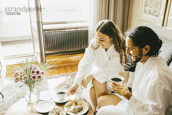 Hochwinkelansicht eines Paares im Bademantel beim Frühstück im Hotelzimmer