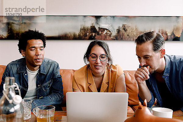 Kollegen arbeiten gemeinsam am Laptop  während sie im Kreativbüro auf dem Sofa sitzen