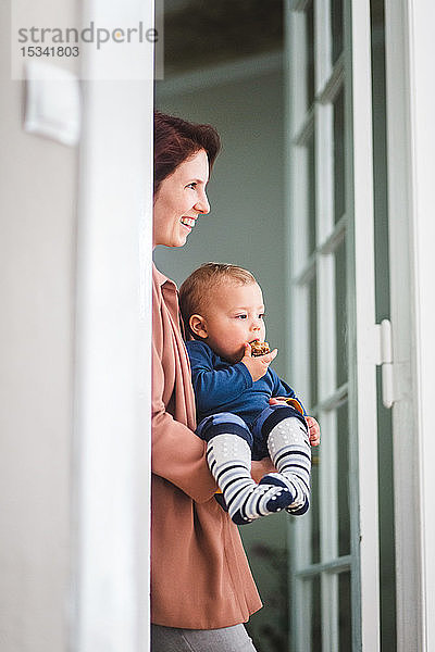Lächelnde Mutter mit Sohn schaut weg  während sie am Hauseingang steht