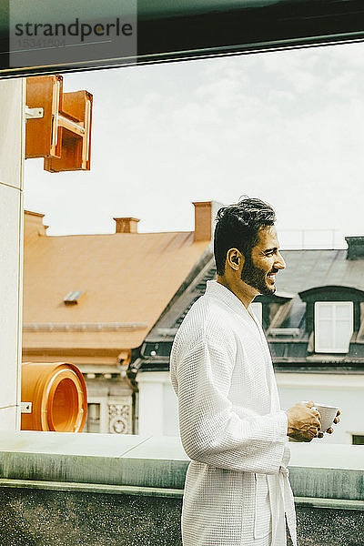 Seitenansicht eines Mannes mit Kaffeetasse auf dem Hotelbalkon
