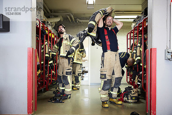 Feuerwehrleute tragen Arbeitsschutzkleidung in der Umkleidekabine  während sie zur Feuerwache aufschauen