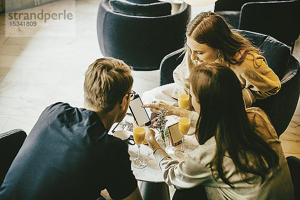 Hochwinkelansicht von Freunden  die ein Smartphone benutzen  während sie im Restaurant etwas trinken