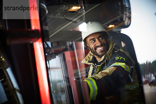 Lächelnder Feuerwehrmann im Feuerwehrauto sitzend durch Glasfenster gesehen