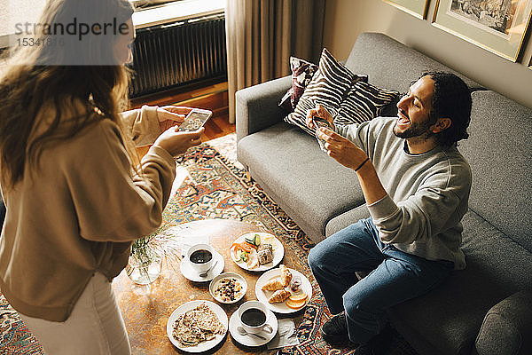 Ehepaar fotografiert Frühstück mit Smartphones im Hotelzimmer