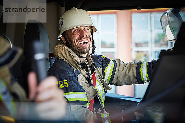 Lächelnder Feuerwehrmann sieht seinen Kollegen an  während er im Feuerwehrauto sitzt