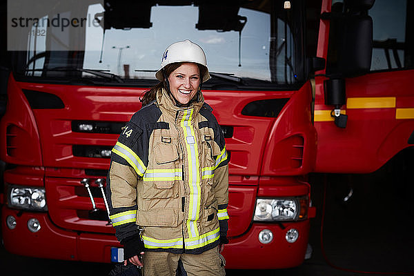 Porträt einer lächelnden Feuerwehrfrau  die vor dem Feuerwehrauto in der Feuerwache steht