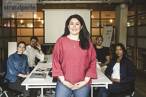 Porträt einer selbstbewussten Geschäftsfrau  die mit dem Team im Hintergrund im Sitzungssaal steht
