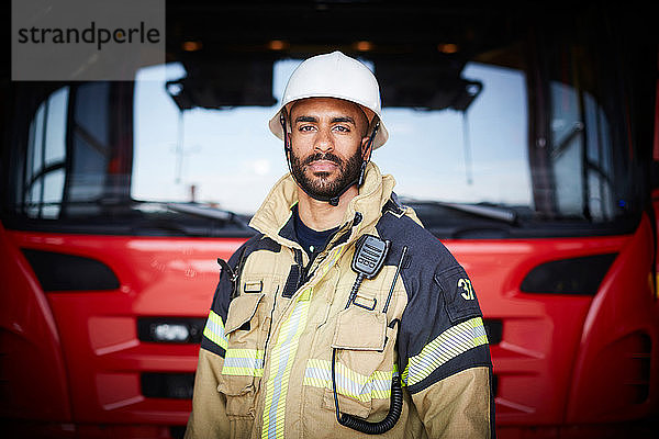 Porträt eines selbstbewussten Feuerwehrmannes  der vor dem Feuerwehrauto in der Feuerwache steht